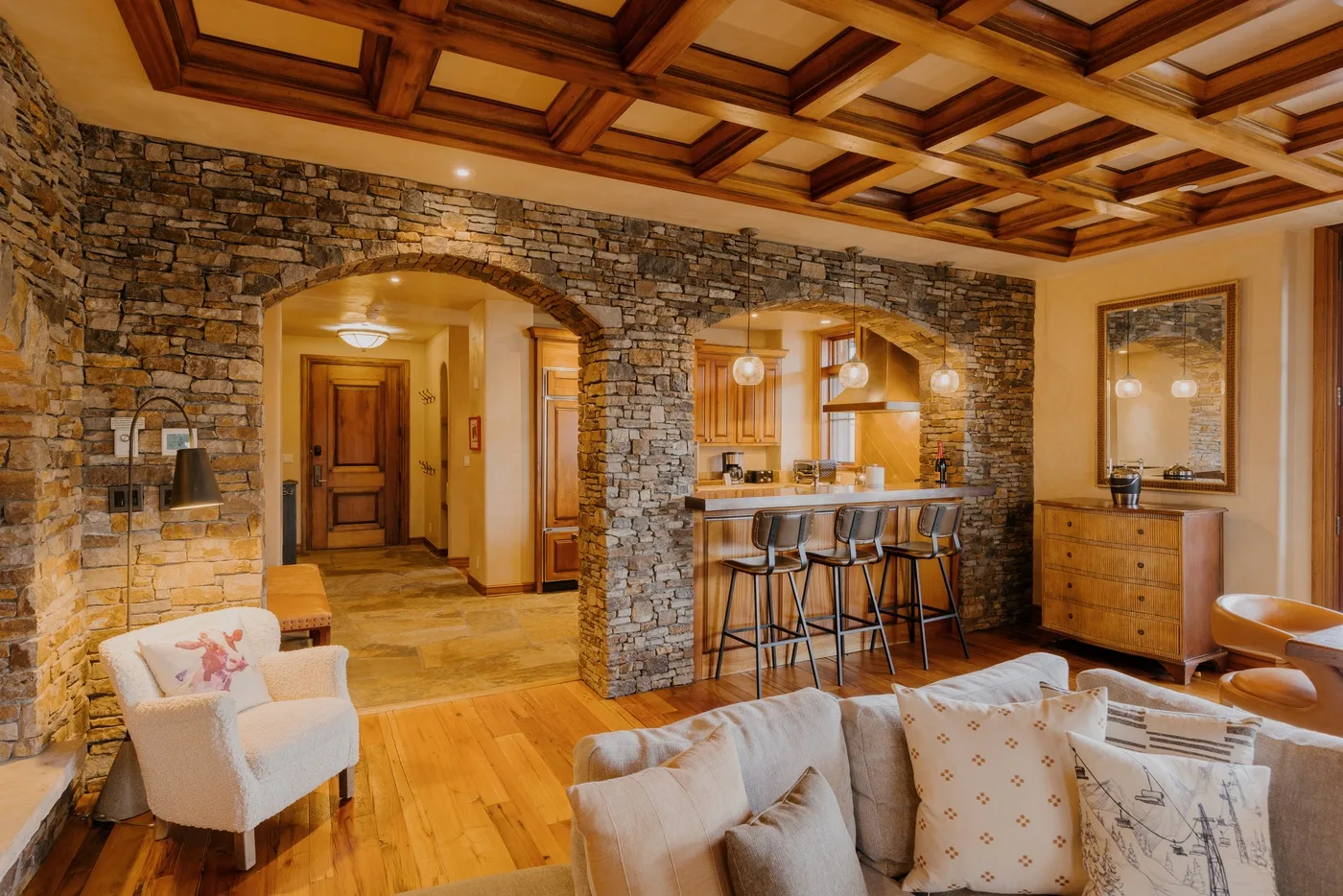 A warm living room opens onto a stone archway and a kitchen counter.
