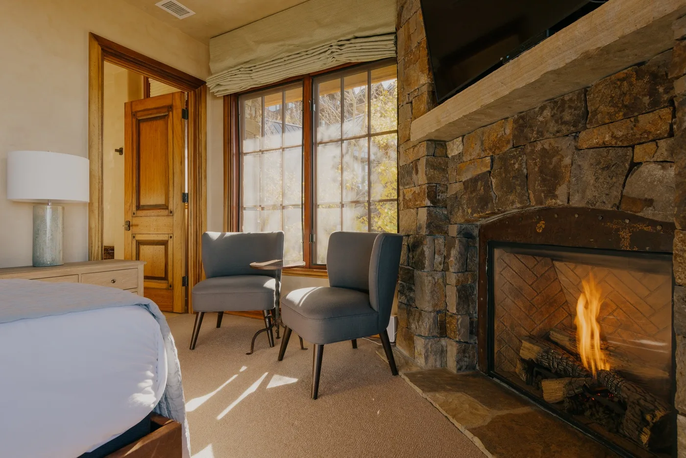 A bedroom sitting area with two chairs beside a stone fireplace and large window.