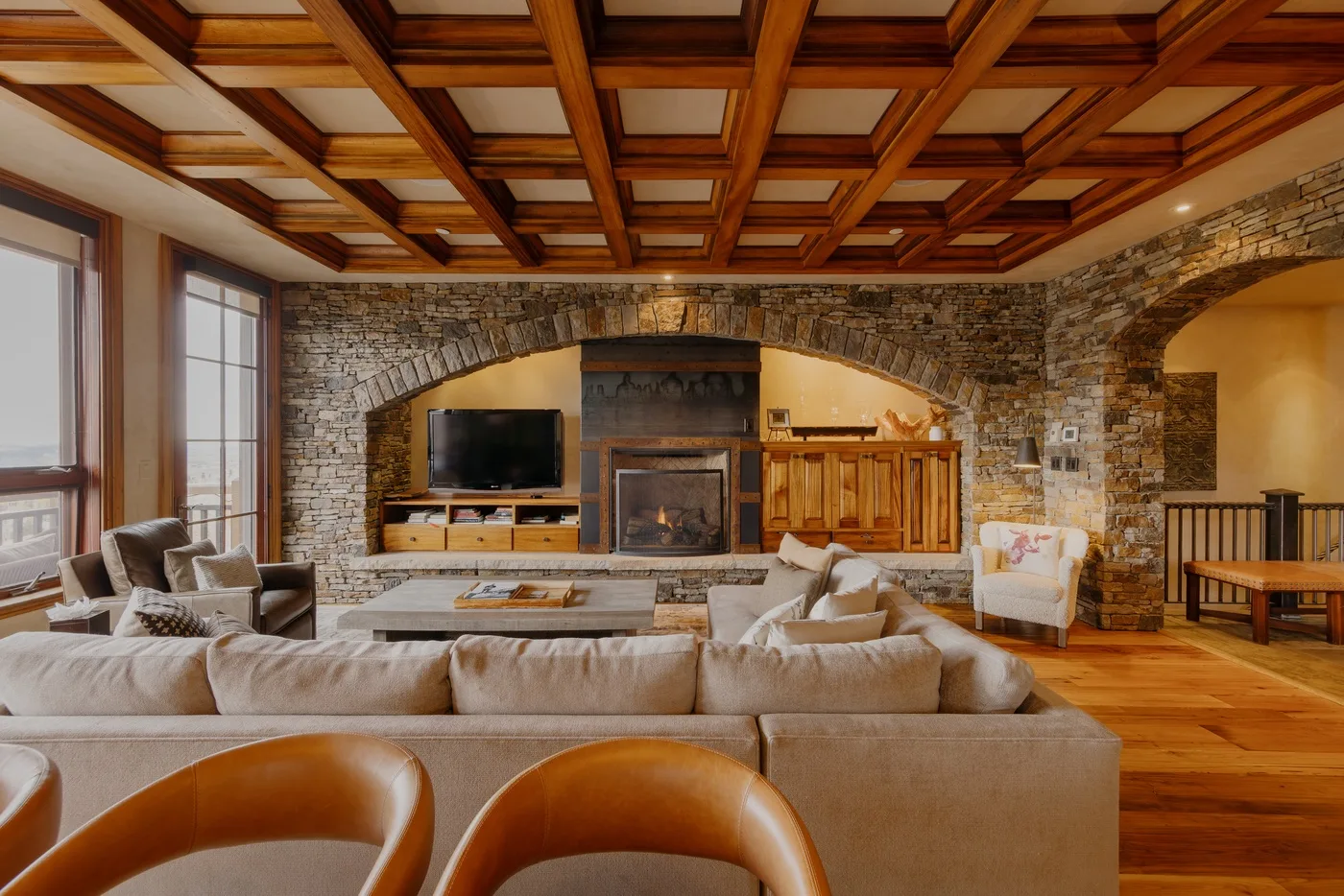 A spacious living room with a stone fireplace, television, and wood-beamed ceiling.