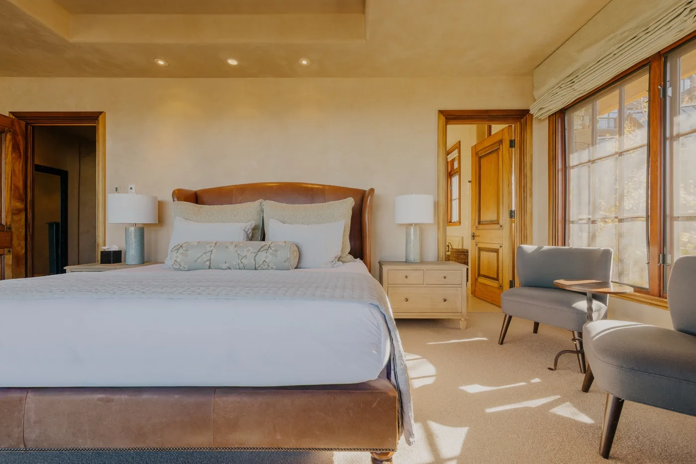 A bedroom with a large bed and seating beside broad windows.