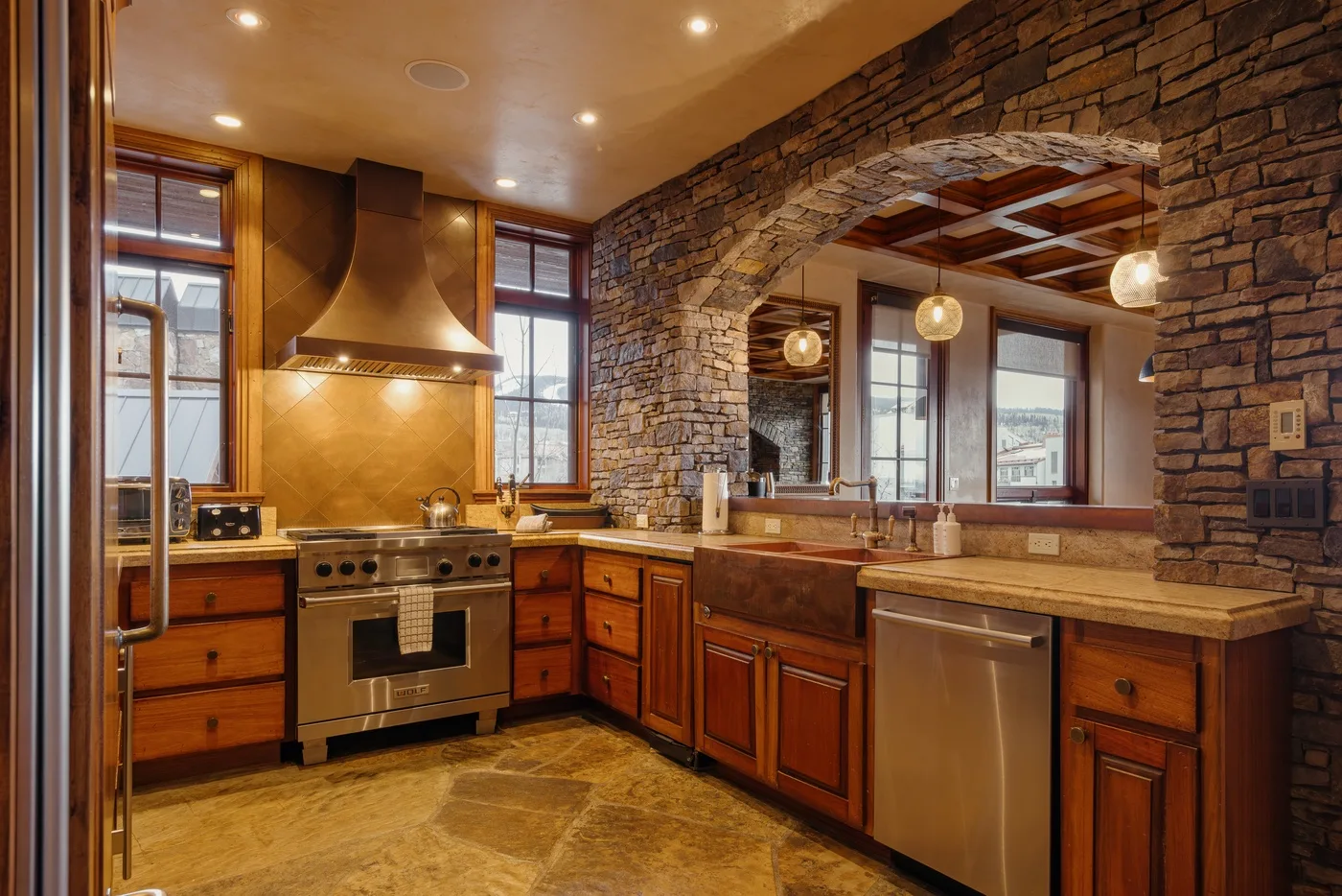 A warm kitchen with wooden cabinets, stone walls, and a stainless steel range.