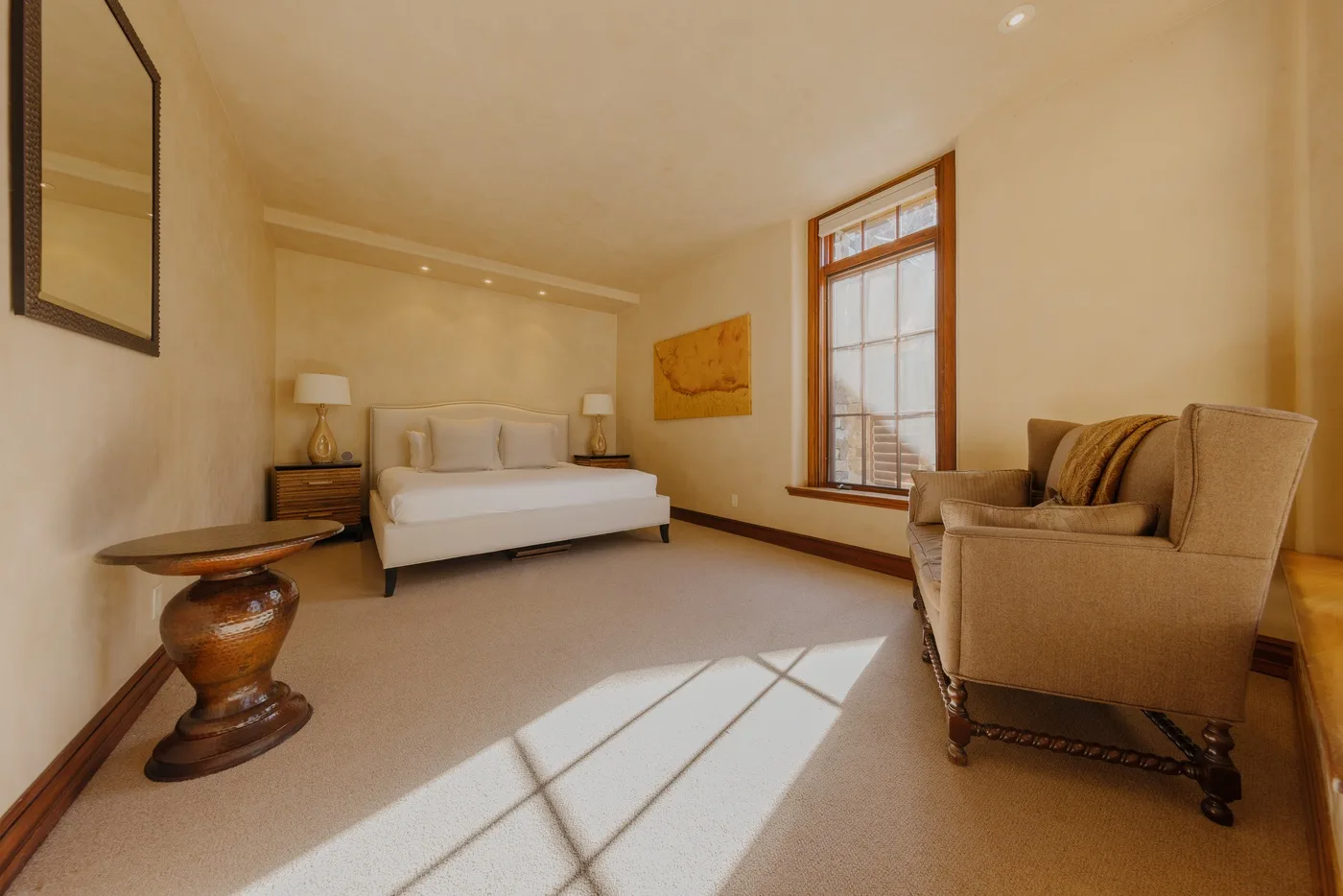 A bedroom with a bed, armchairs, and a large sunlit window.