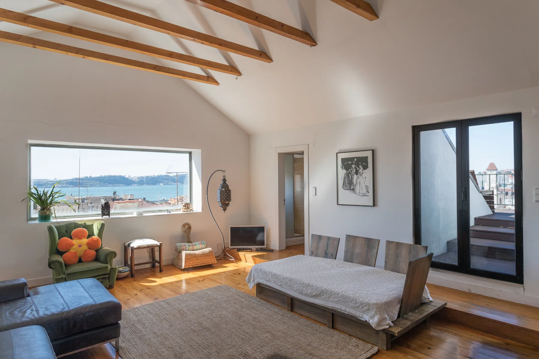 Una luminosa sala de estar y comedor tiene vigas expuestas y una gran ventana con vistas al agua.