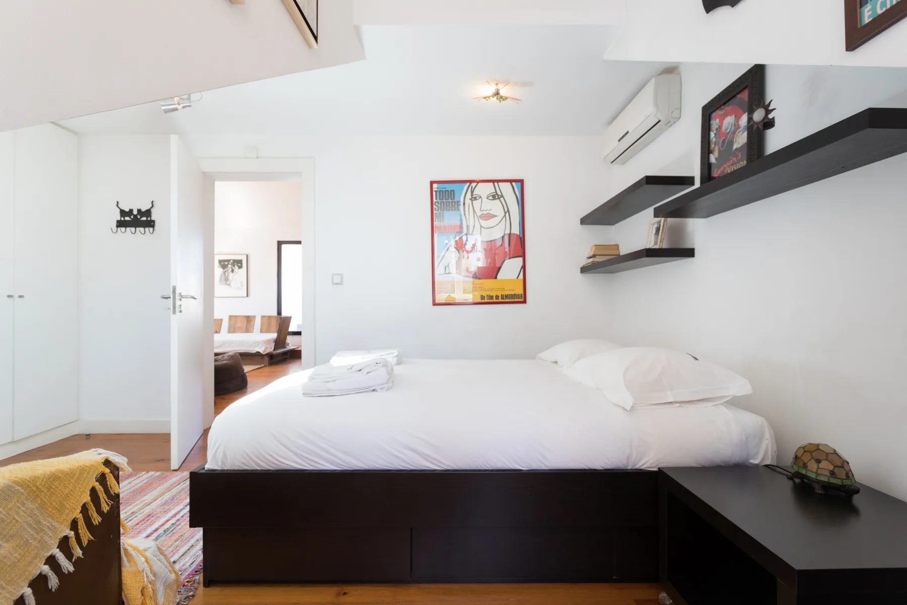 Un dormitorio con una cama tendida, estantes de pared y una obra enmarcada.