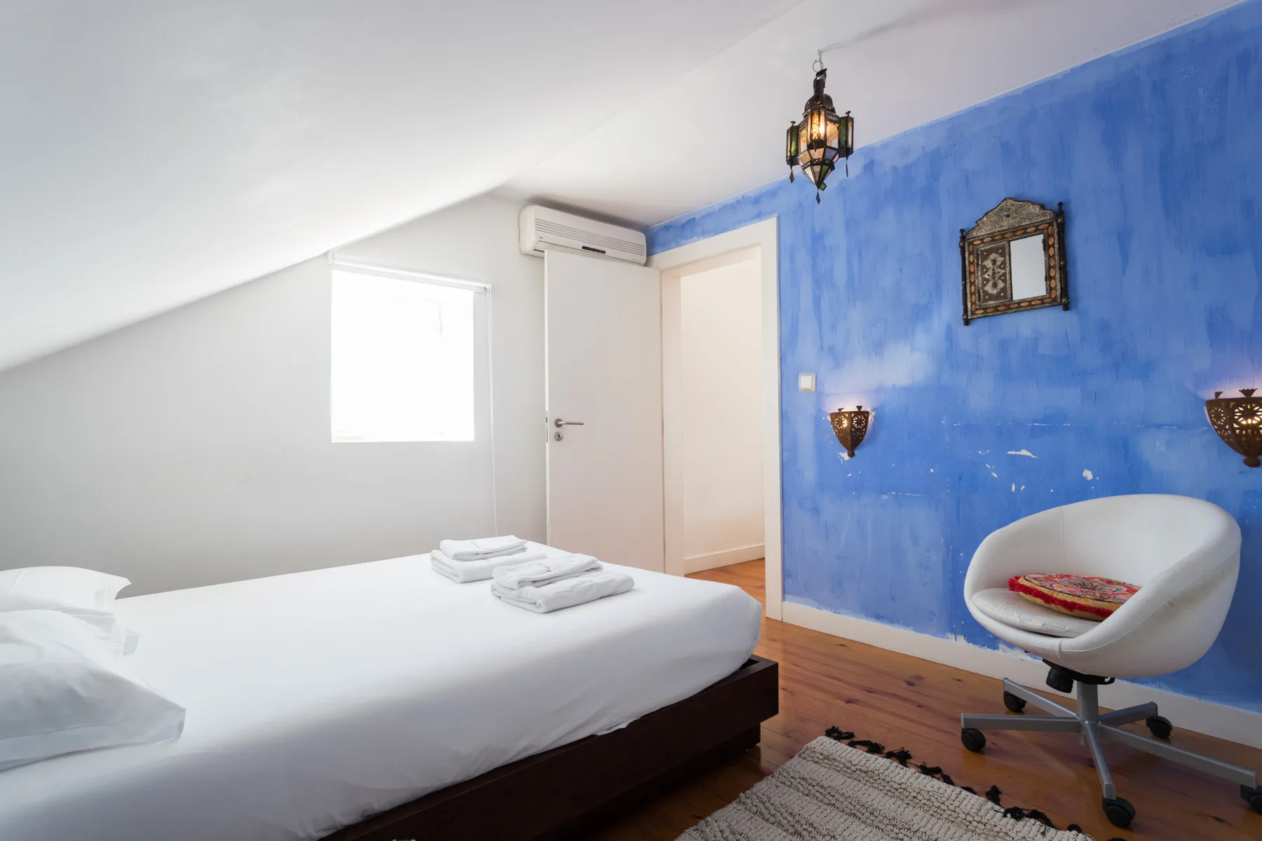 Un dormitorio con techo inclinado, una cama y una pared azul.