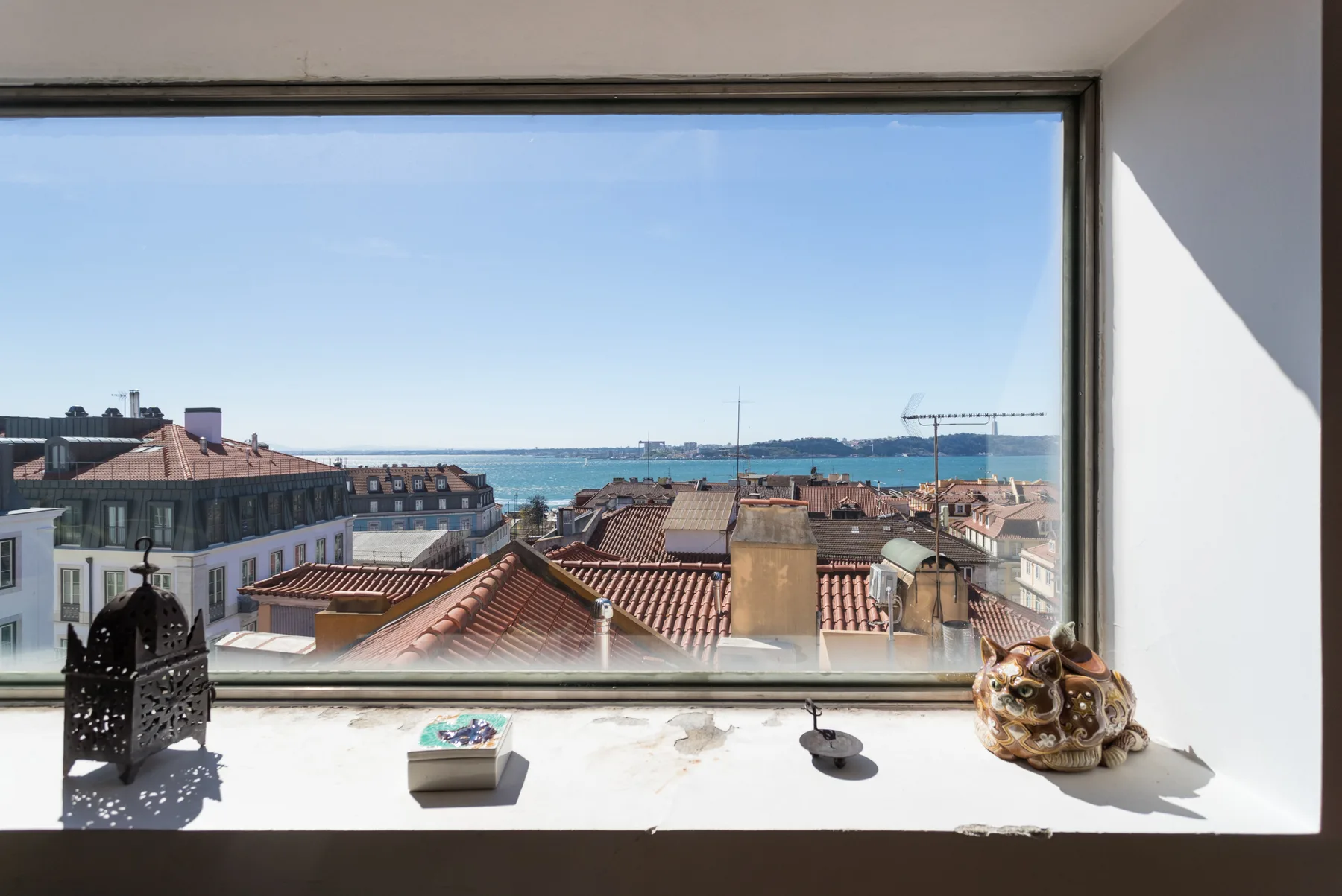 Una gran ventana da a tejados rojizos y al paseo marítimo azul.