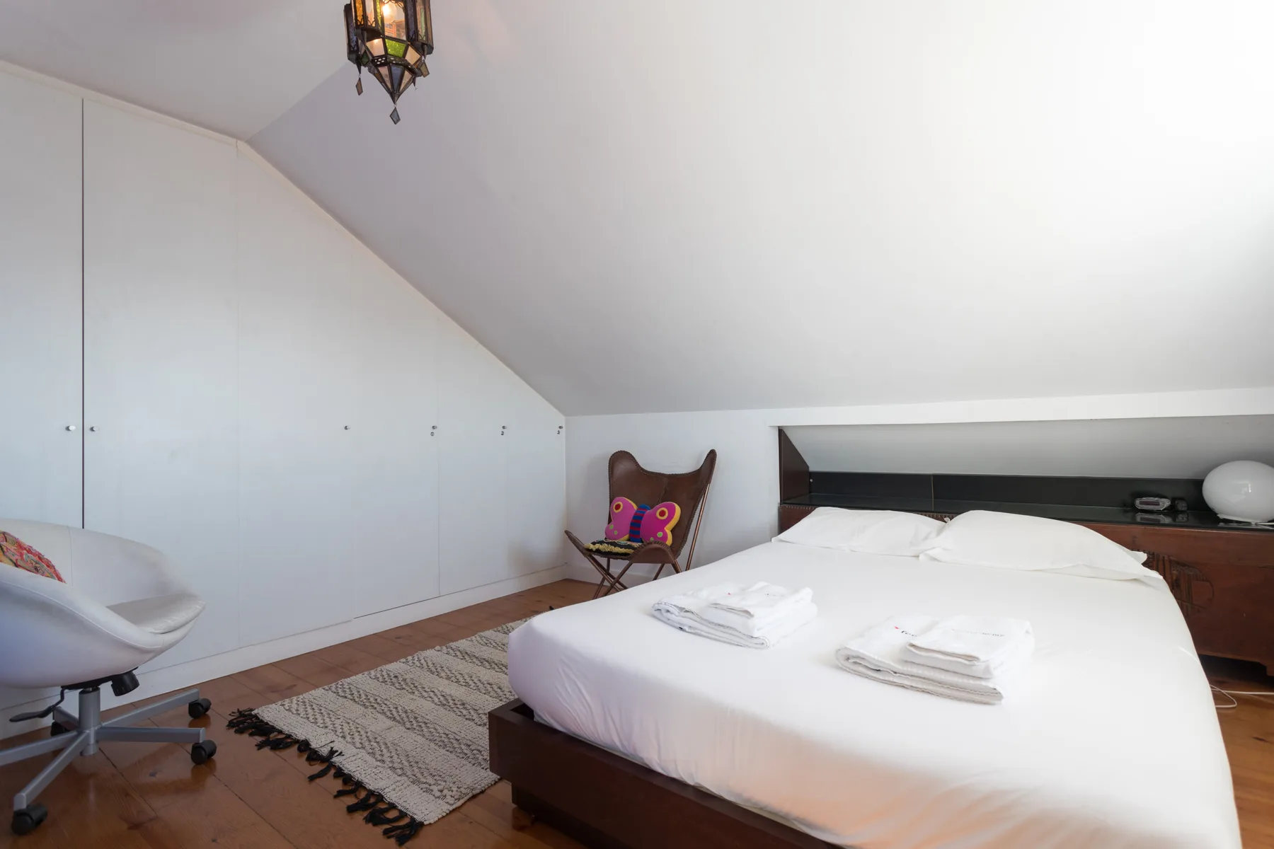 Un dormitorio con una cama, una estantería baja y un techo inclinado.