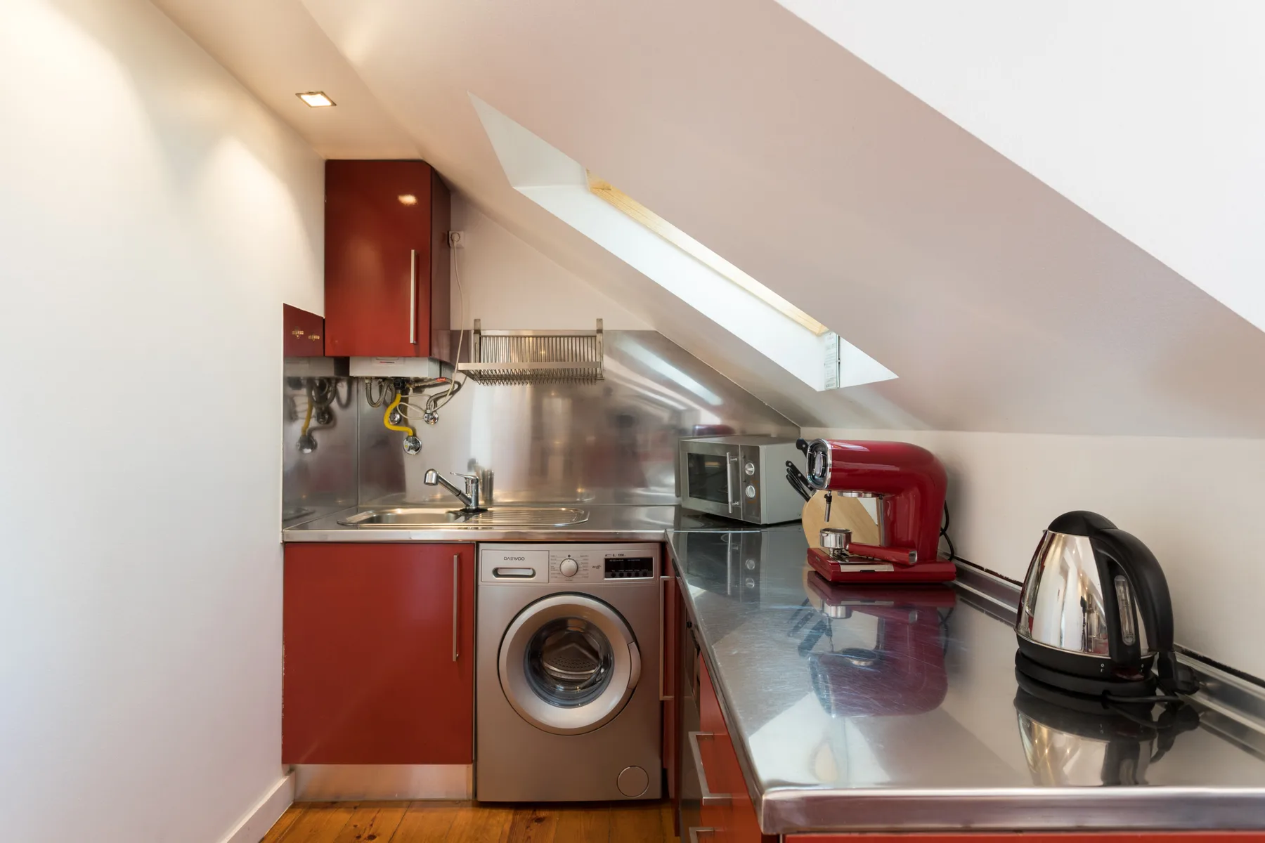 Una cocina compacta con armarios rojos, una lavadora y electrodomésticos sobre la encimera.