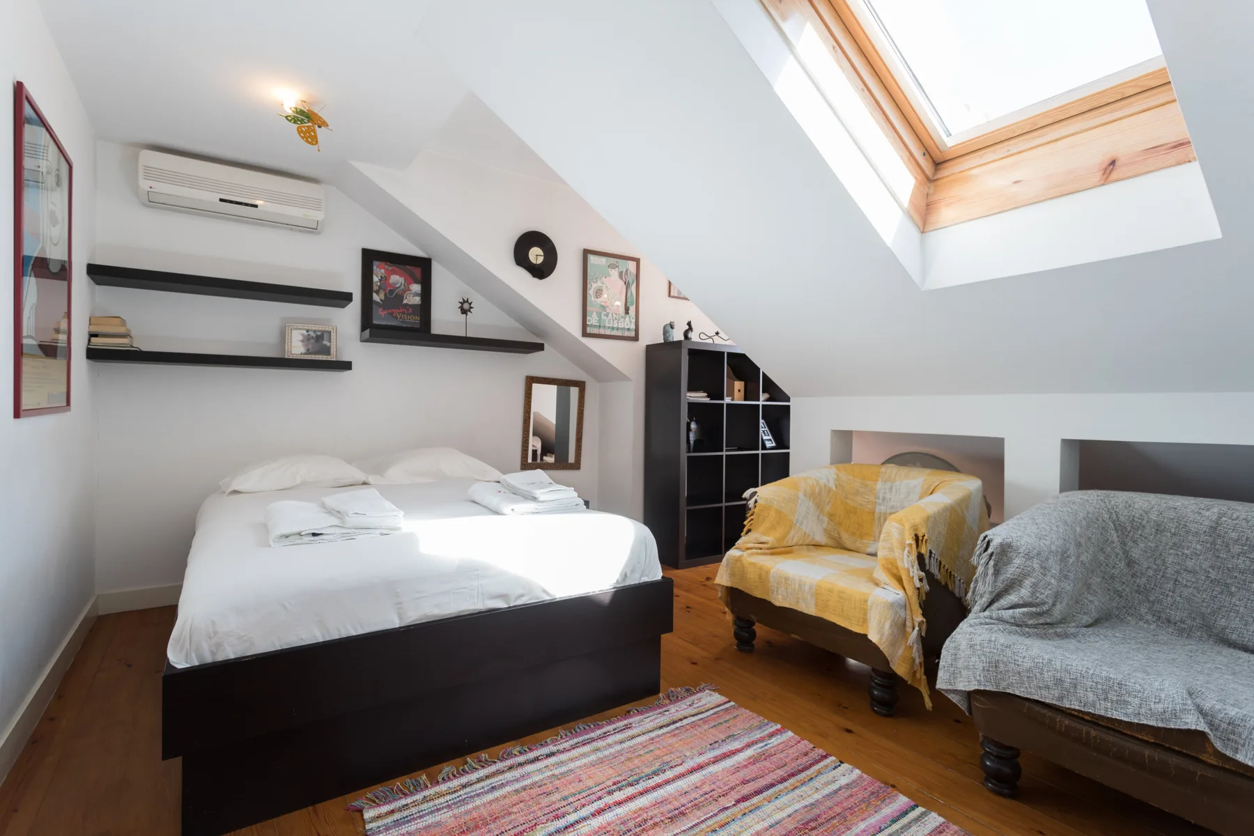 Un dormitorio abuhardillado luminoso con una cama y asientos bajo una claraboya.