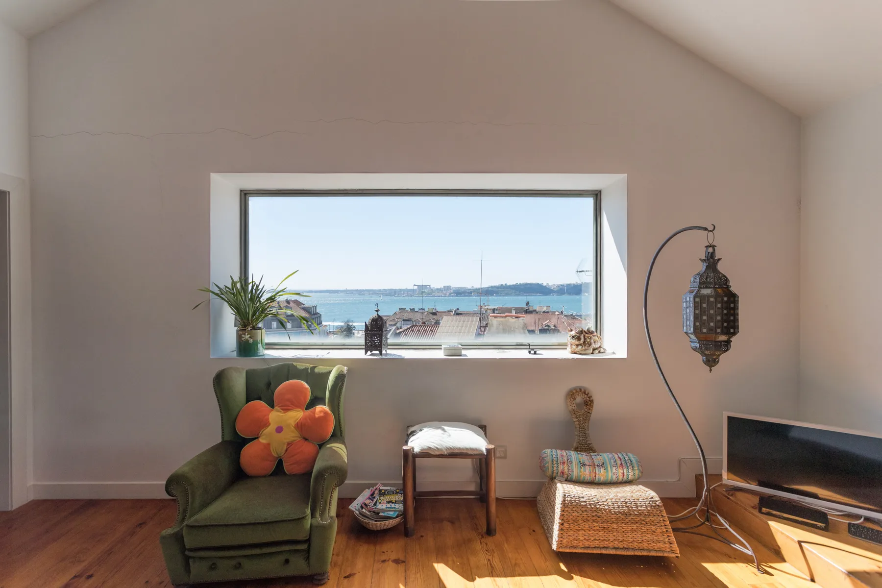 Una zona de estar con un sillón verde junto a una ventana amplia con vistas al agua.