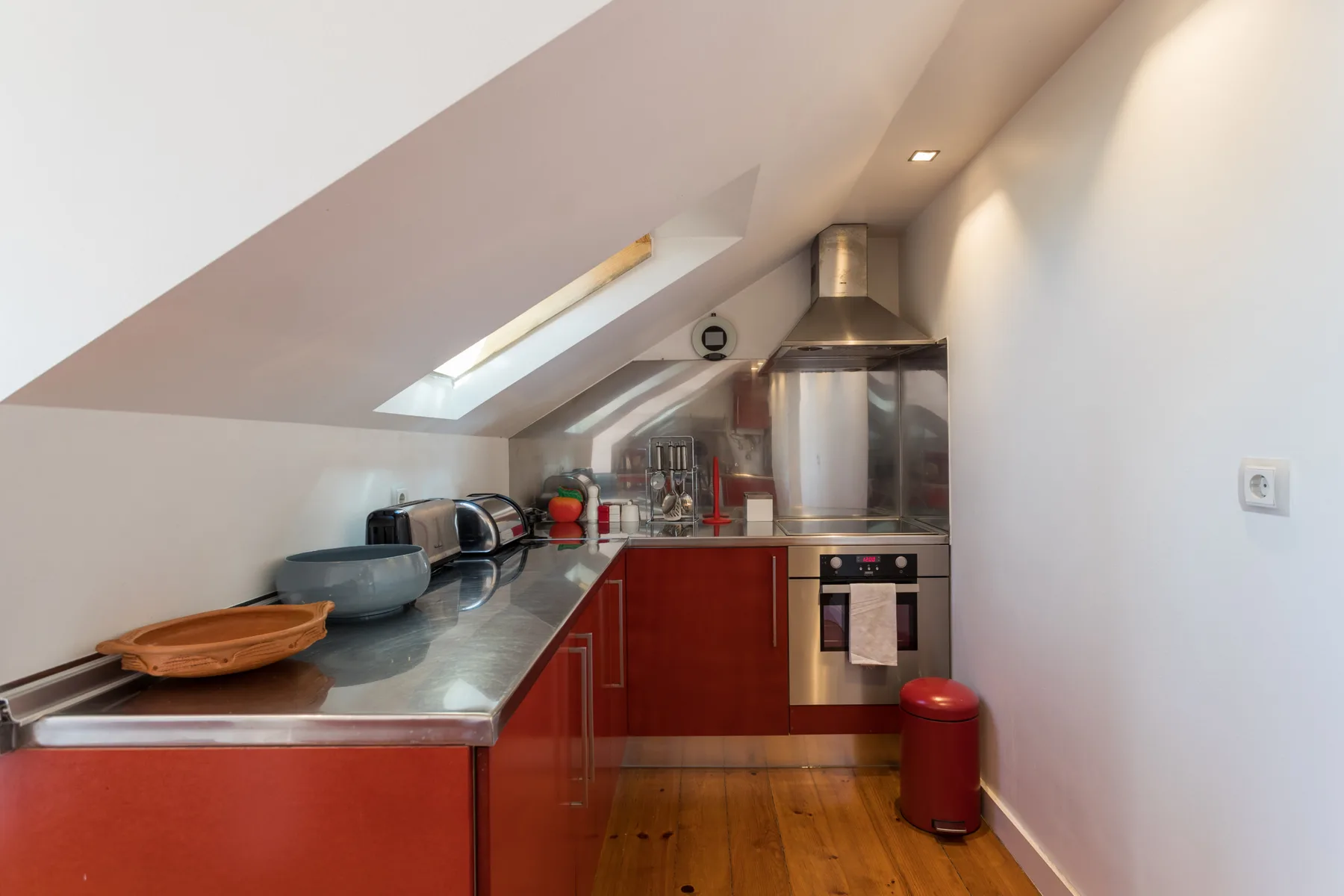 Una cocina compacta con gabinetes rojos y una encimera de acero inoxidable.