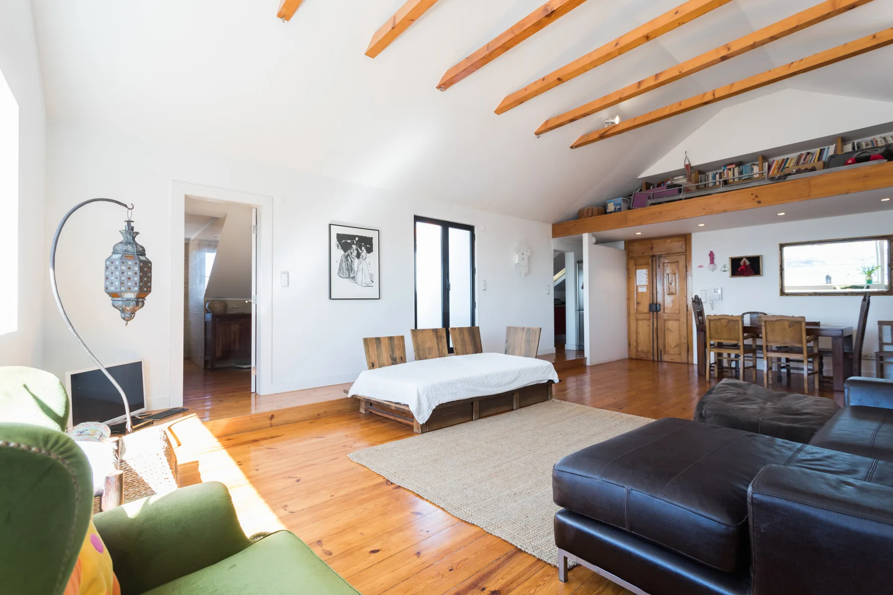 Una sala luminosa con comedor, vigas de techo a la vista y suelo de madera.