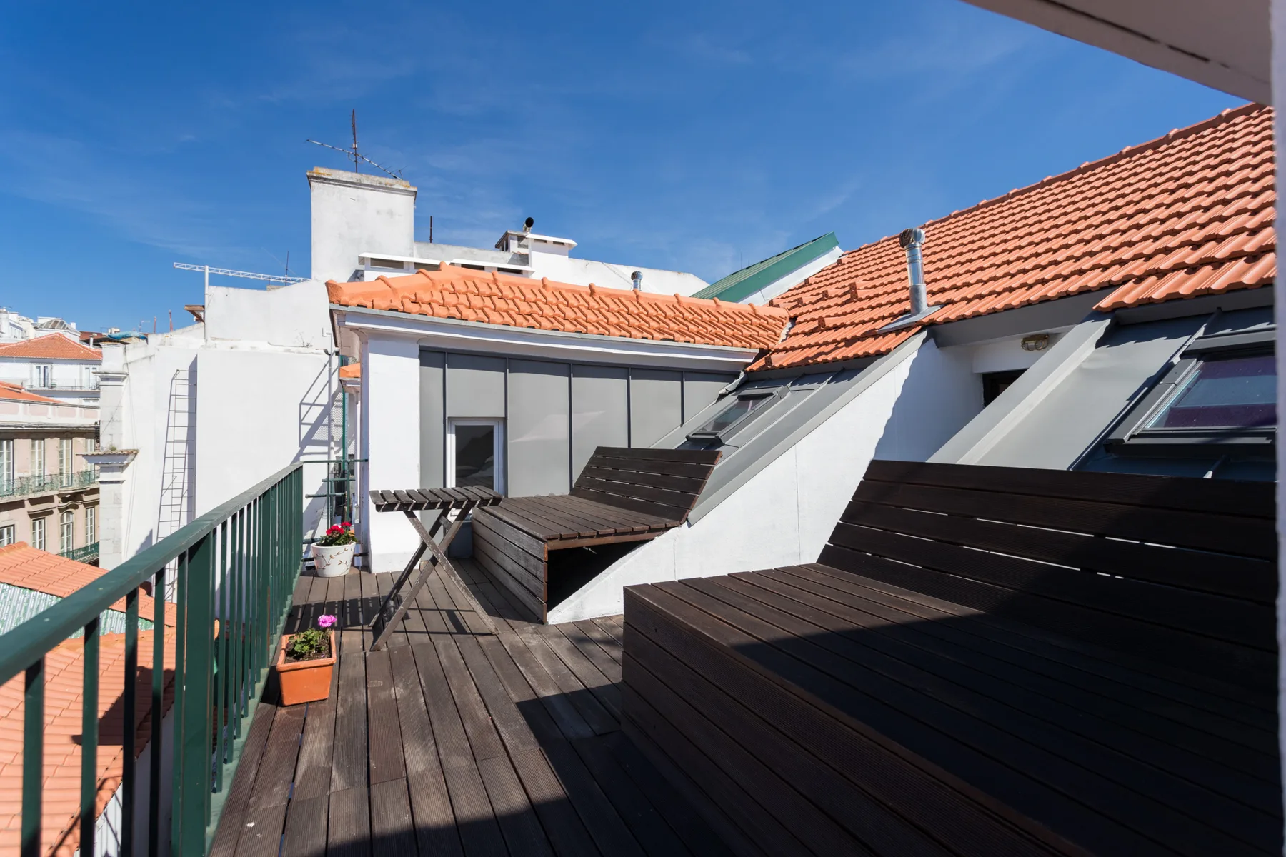 Una terraza en la azotea con tarima de madera, asientos y ventanas inclinadas en el tejado.