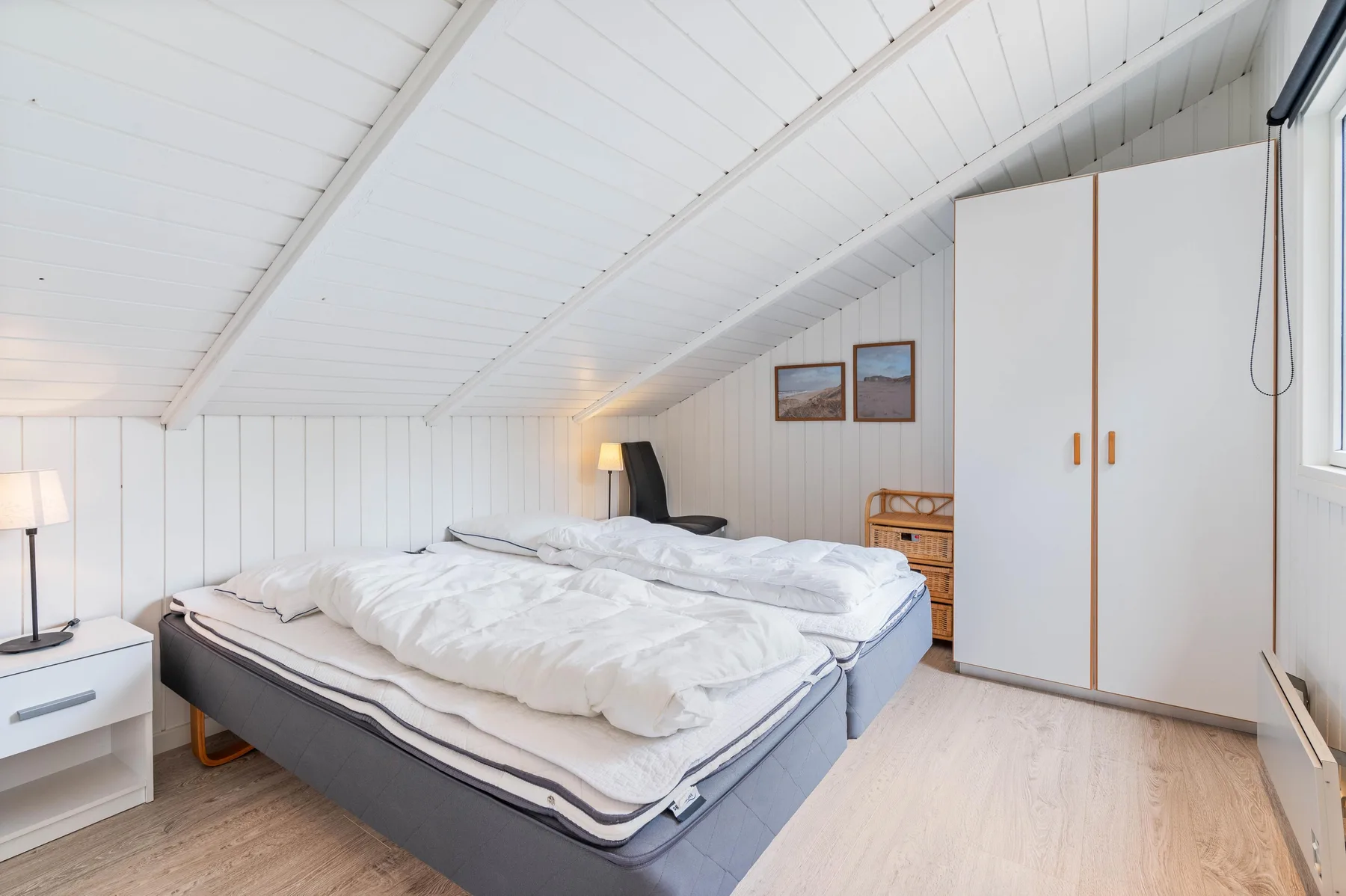 A bedroom with a large bed, bedside tables, and a white sloped ceiling.
