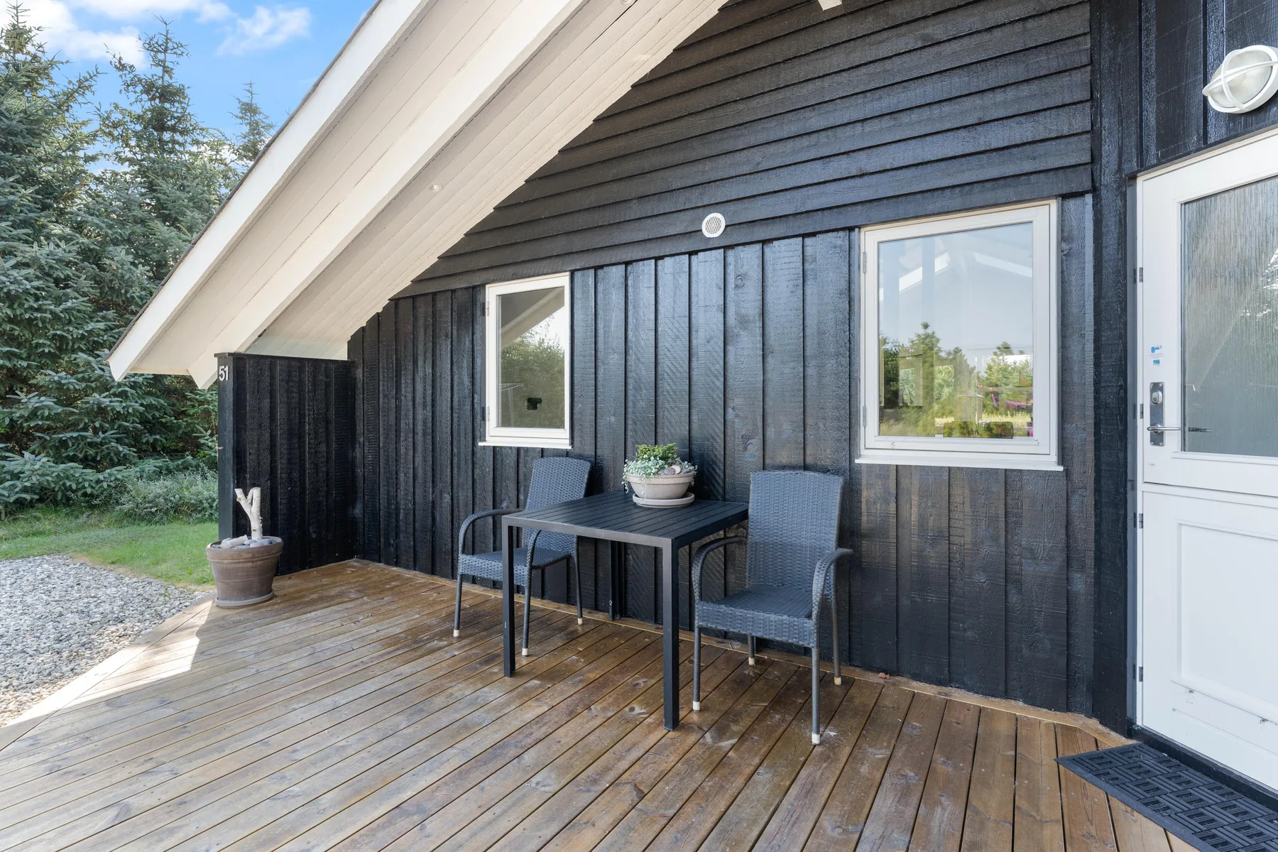 An outdoor seating area sits on a wooden deck beside a dark-sided building.