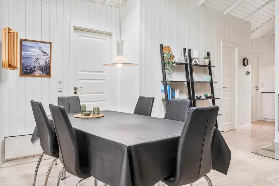 A dining area with a long table, dark seating, and white paneled walls.
