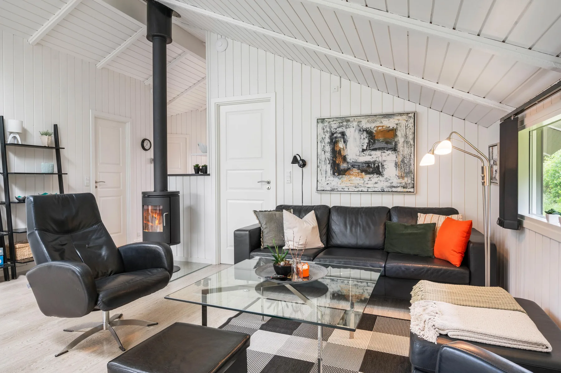 A living room with dark seating, a glass coffee table, and a wood-burning stove.