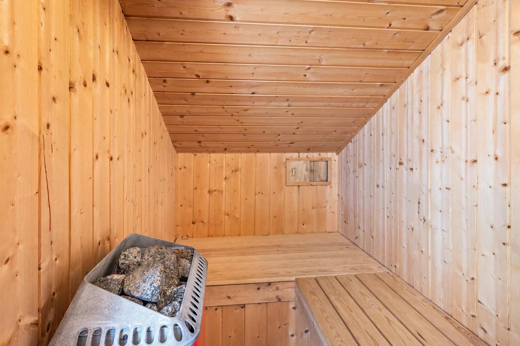 A wood-paneled sauna room with a stone-filled heater and tiered wooden benches.