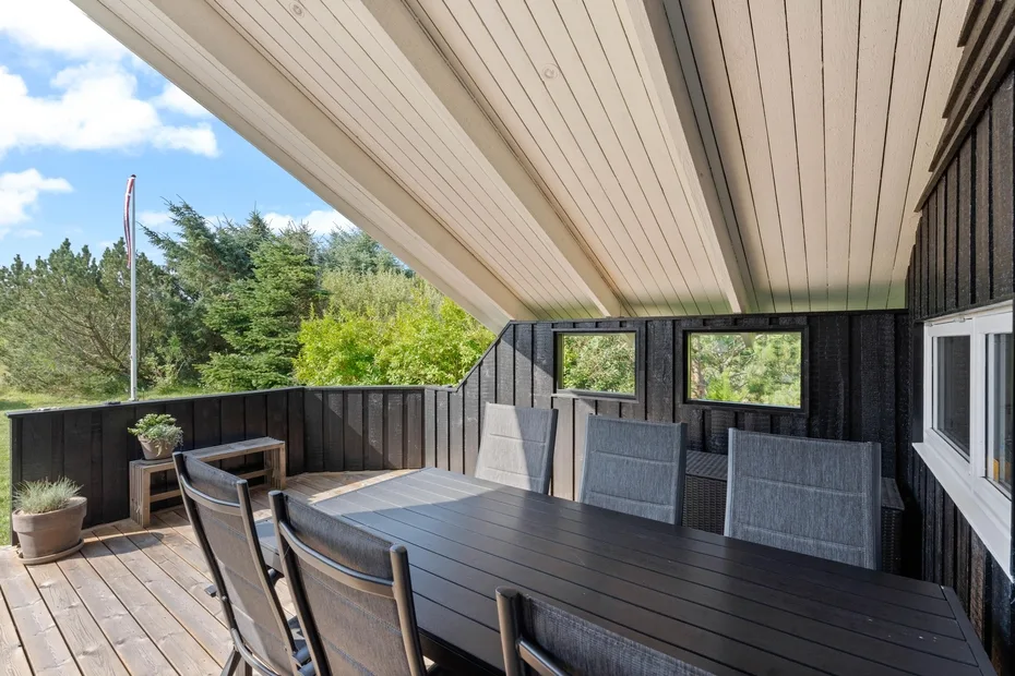 A covered outdoor dining area with a table and seating beside trees.