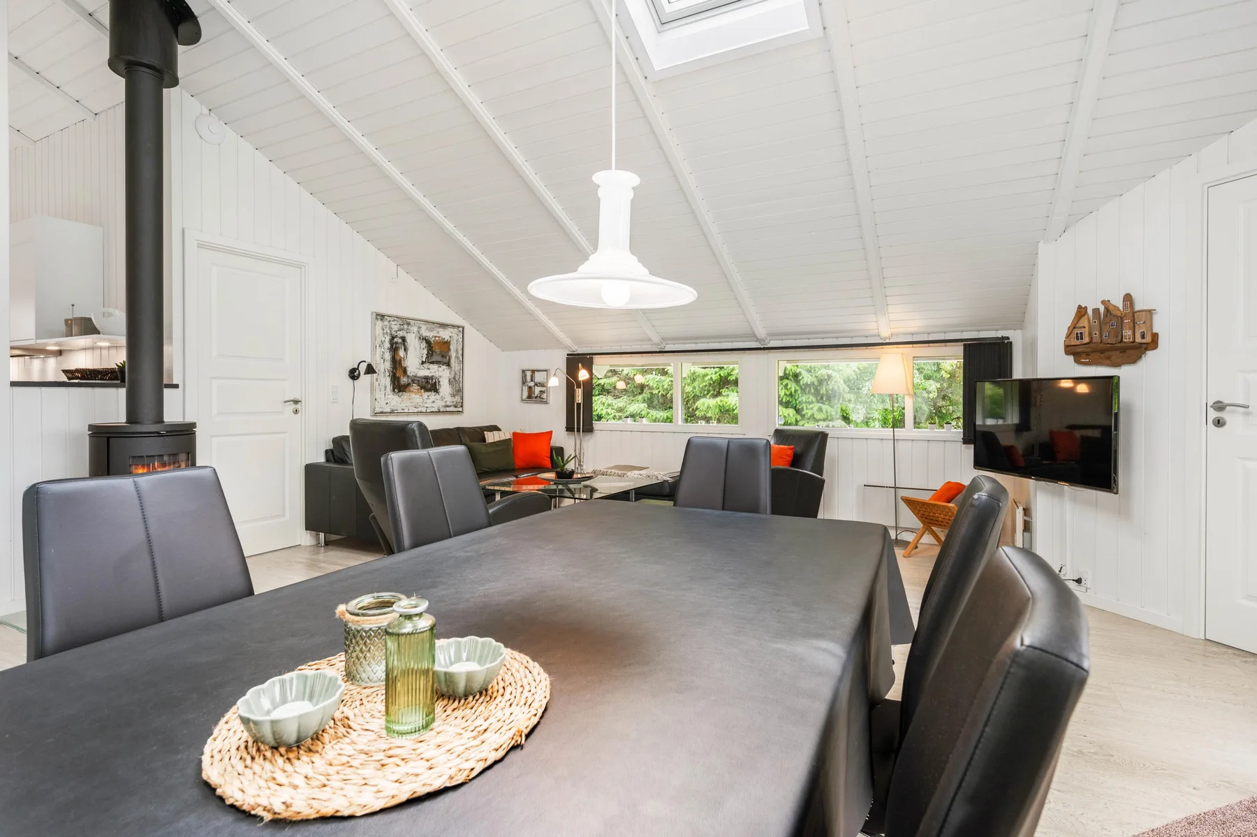A dining area with a long table and seating, beside a living area with a television.