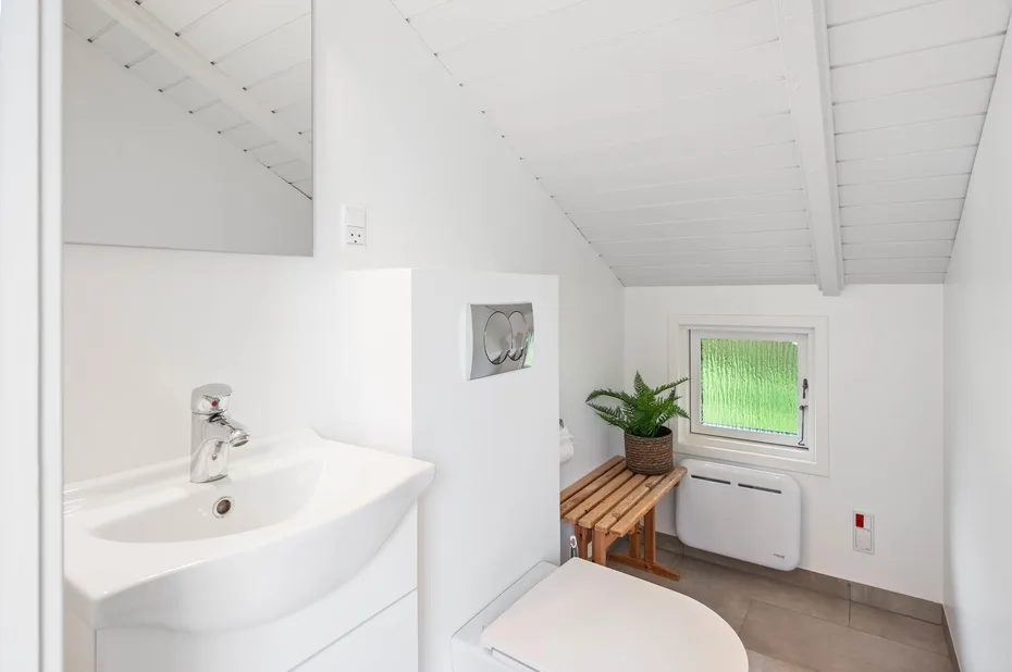 A bright bathroom with a sink, a window, and a potted plant.
