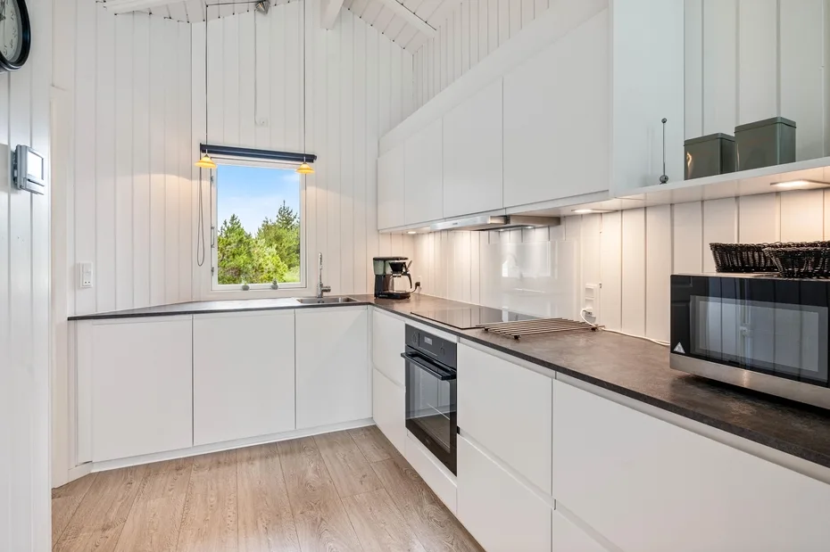 A bright kitchen with white cabinets, dark countertops, and a window overlooking greenery.