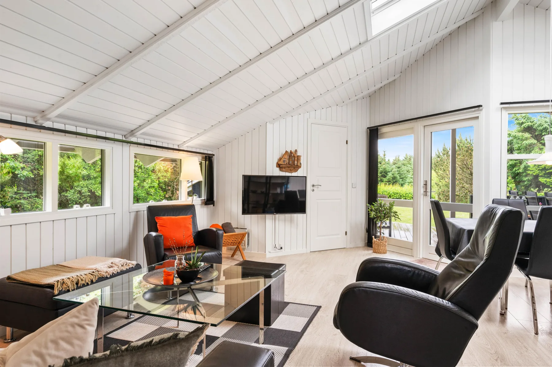 A bright living room with a glass coffee table and seating beside large windows.