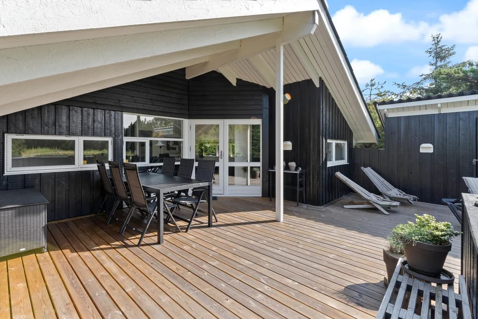 A wooden deck beside a dark-sided house has outdoor seating and lounge chairs.