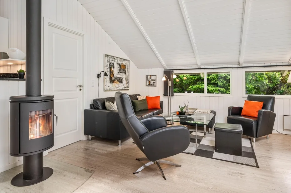 A bright living room with black seating, a glass coffee table, and a wood-burning stove.