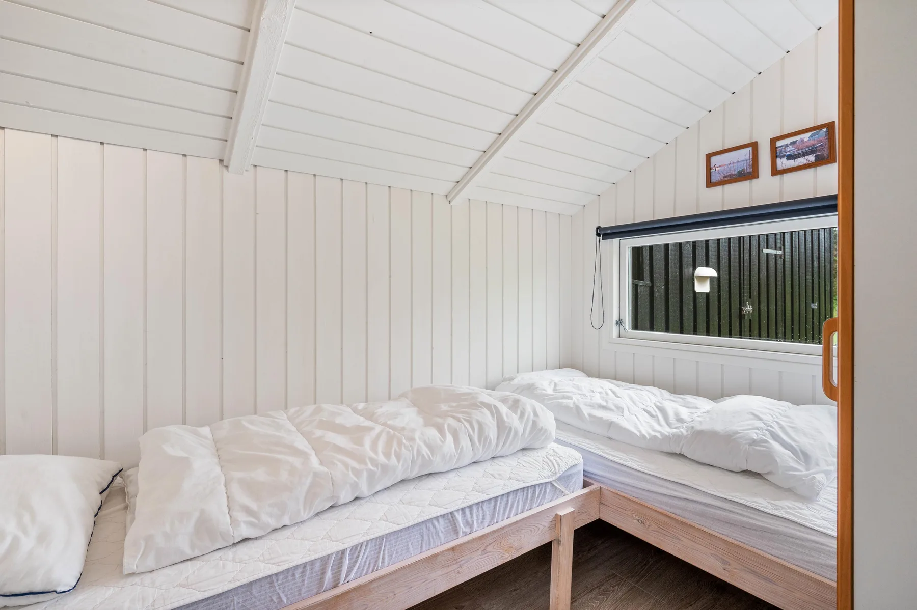 A bedroom with two beds beneath a sloped white-paneled ceiling.