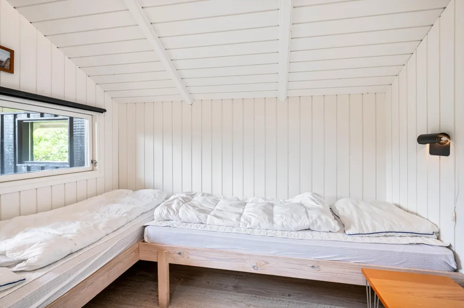 A bright bedroom with white bedding and a small window.