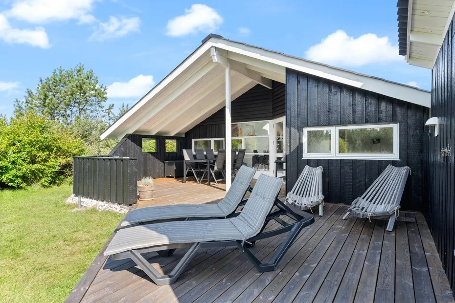 A wooden deck beside a dark house has lounge seating and a covered dining area.