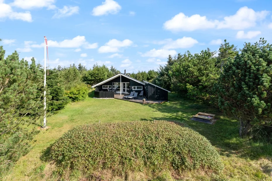 A dark house sits beyond a grassy yard, surrounded by trees.