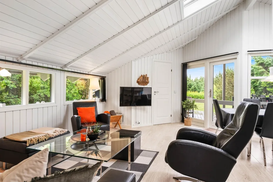 A bright living room with seating, a coffee table, and windows overlooking greenery.
