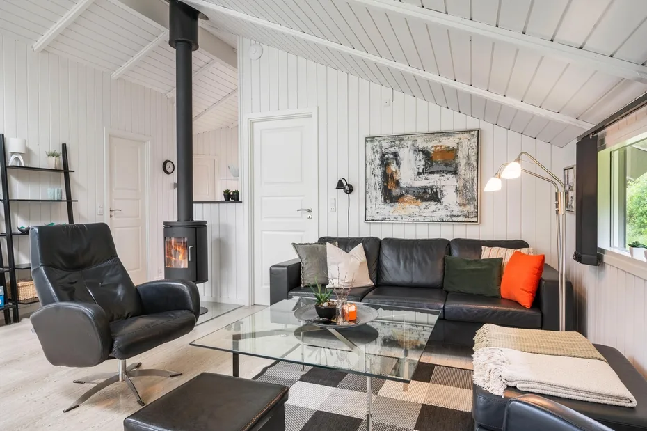 A bright living room with a black sofa, a glass coffee table, and a freestanding stove.