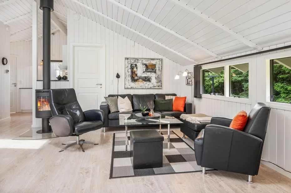 A bright living room with dark seating around a coffee table beneath a sloped ceiling.