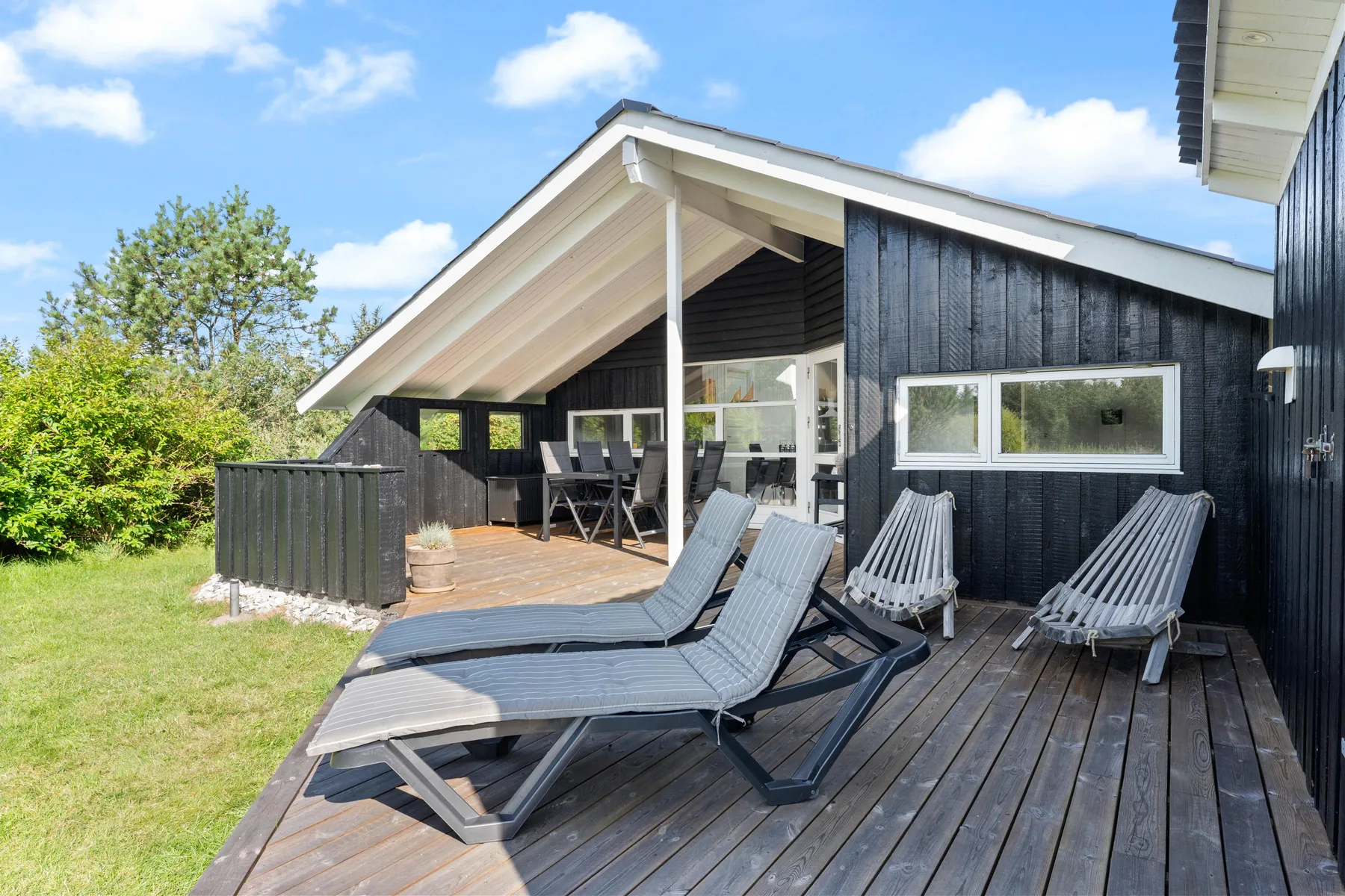A dark-sided house with an outdoor deck, lounge seating, and a covered dining area.