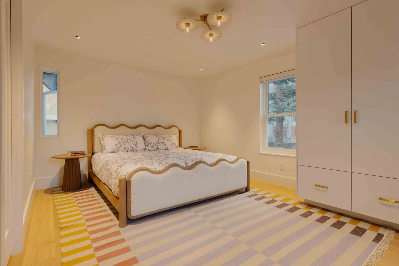 Un dormitorio luminoso con una cama estampada y una alfombra de rayas coloridas.