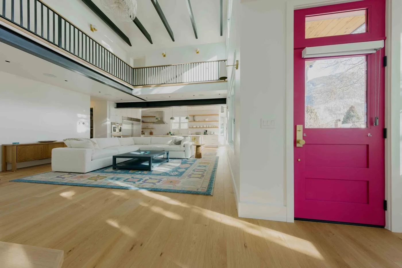 Una sala de estar diáfana y luminosa con asientos blancos y una puerta de entrada magenta.