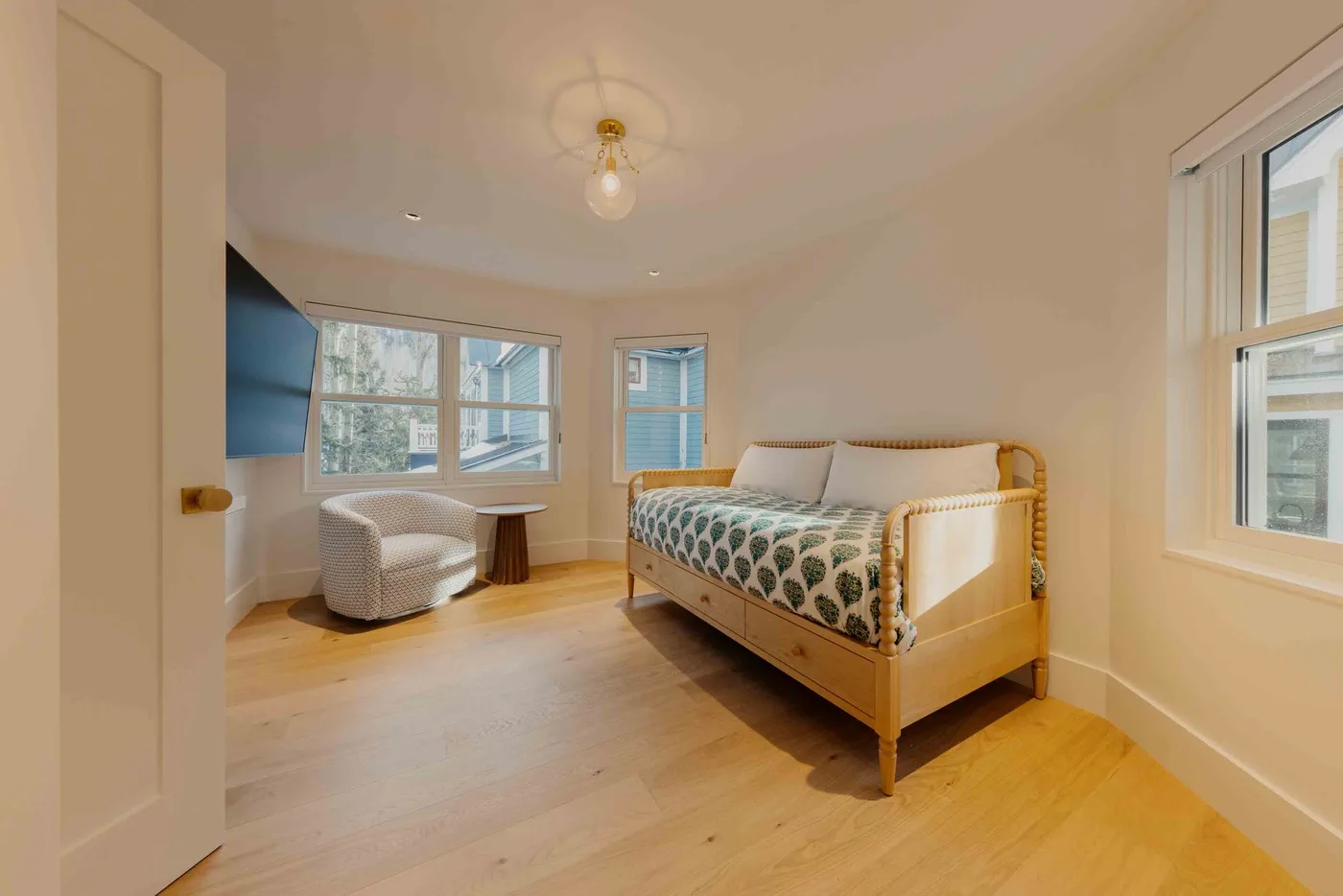 Un dormitorio luminoso con una cama de madera, ropa de cama estampada y ventanas.