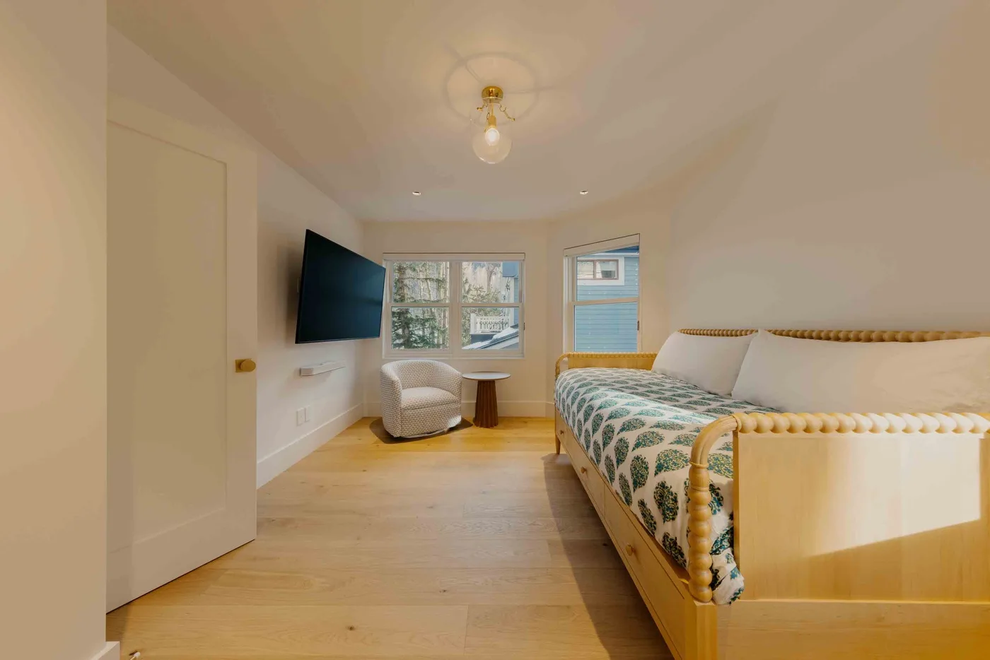 Un dormitorio con una cama, un televisor en la pared y ventanas.