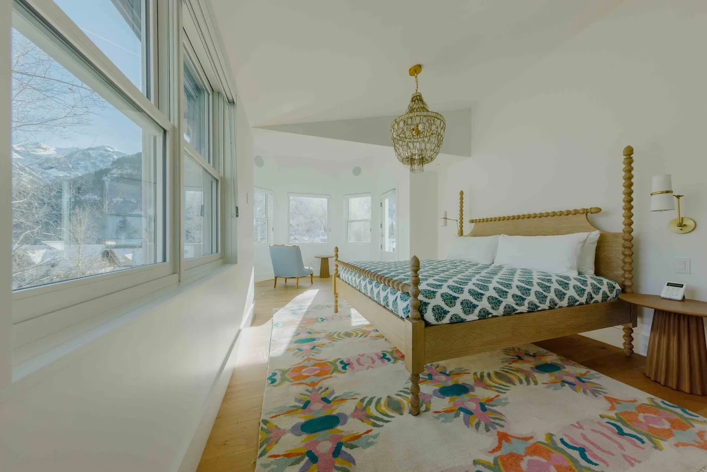 Un dormitorio luminoso tiene una cama de madera, ropa de cama estampada y ventanas grandes.