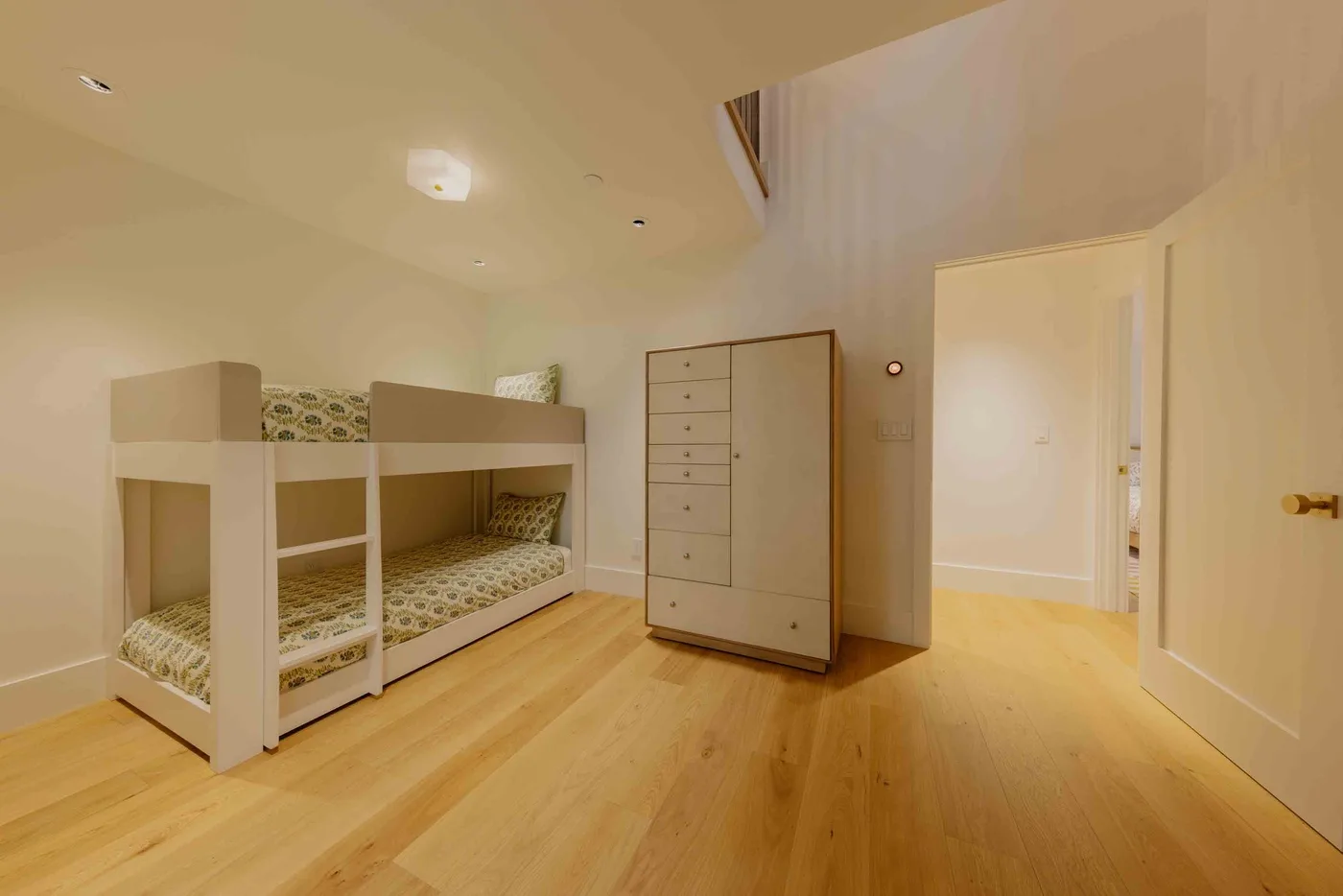 Un dormitorio con literas y una cómoda junto a una puerta abierta.