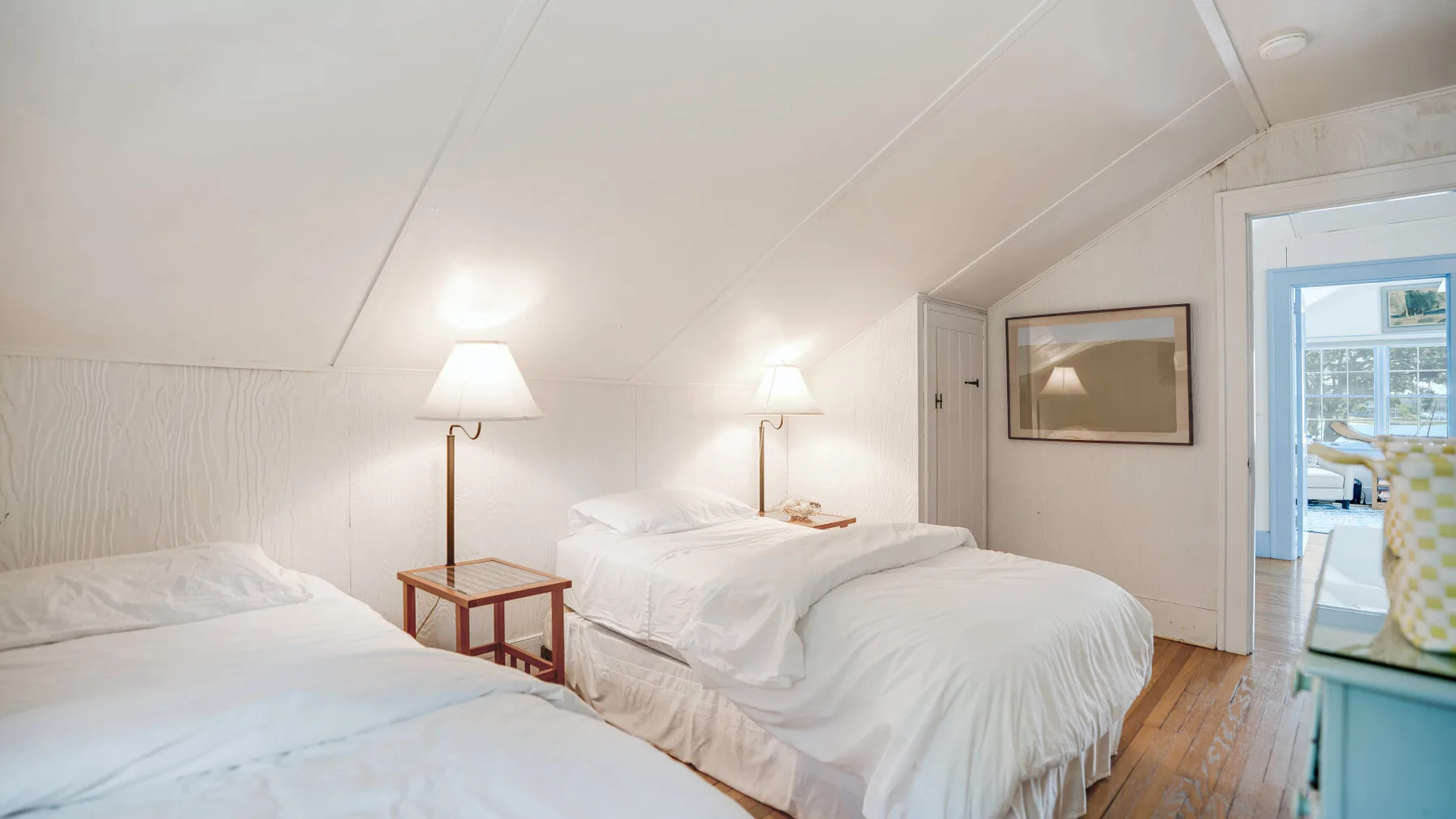 A bright bedroom with white bedding and a small table between the beds.