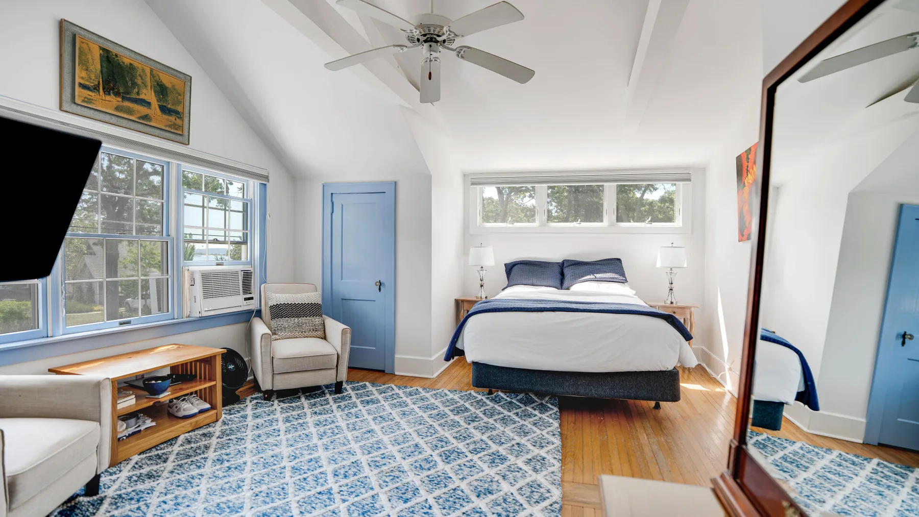 A bright bedroom with a bed, blue door, and patterned rug.