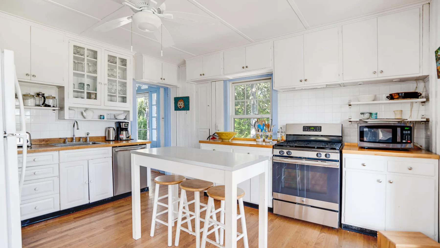 A bright white kitchen with a central island and wooden flooring.