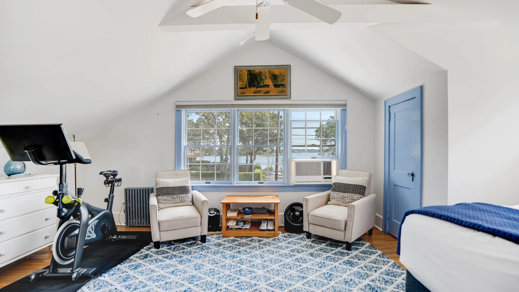 A bright attic room with exercise equipment, seating, and a large window.