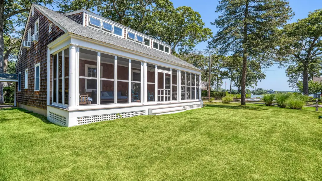 A house with a screened porch stands beside a broad green lawn.