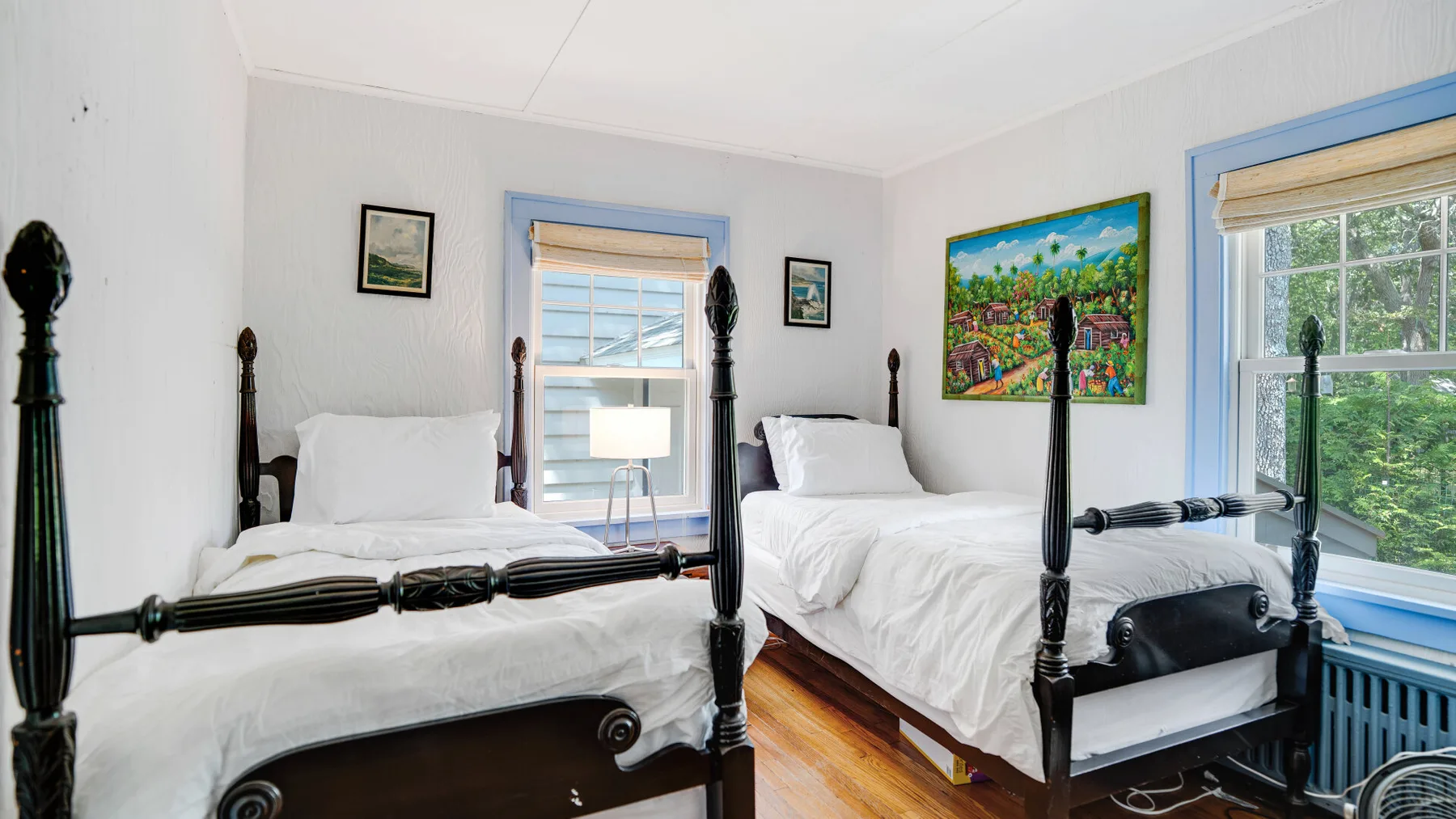 A bedroom with two beds, blue-trimmed windows, and colorful wall art.