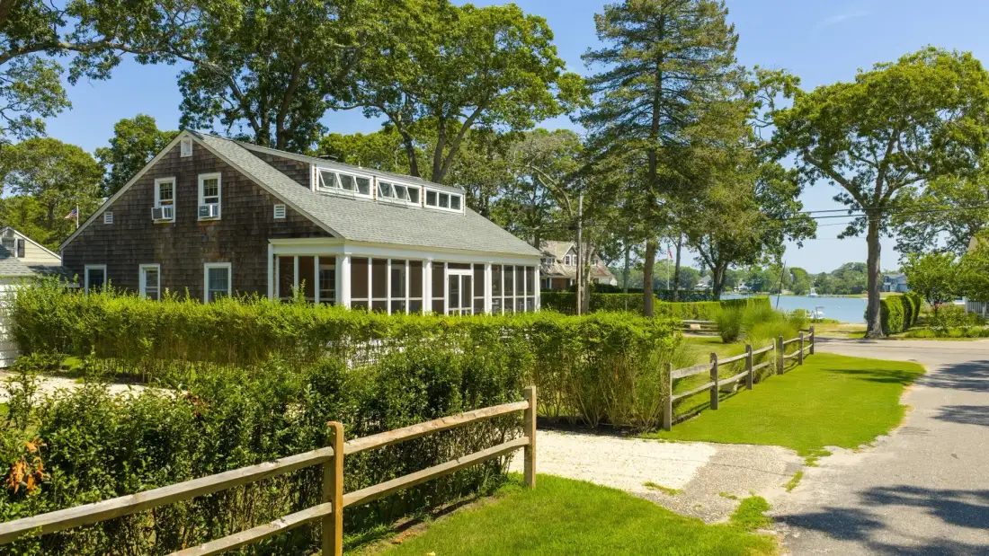 A dark-sided building sits beside a gravel path, wooden fence, and green lawn.